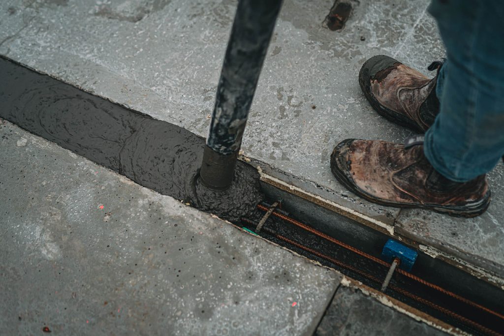 Je ziet hoe een naad van een kanaalplaatvloer gevuld wordt met beton 